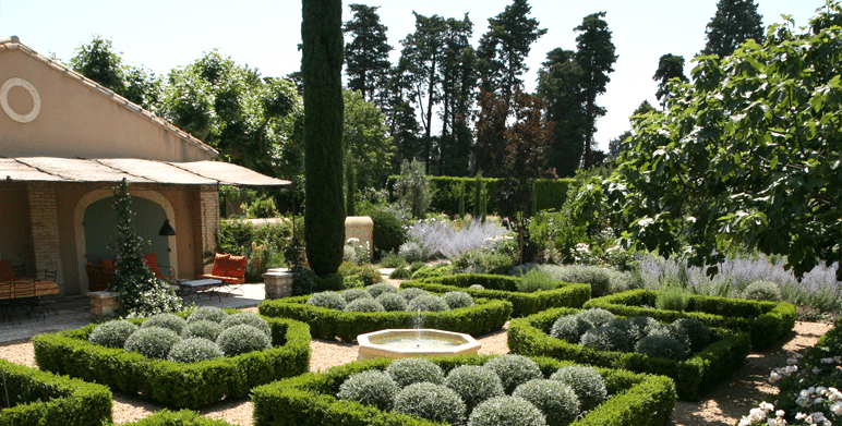 Jardin provençal avec parterres de buis, santolines en boules, fontaine centrale et cyprès élancés.
