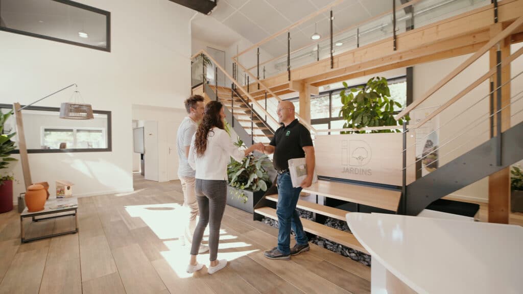 Poignée de main entre un couple et un conseiller ID Jardins dans un showroom paysager moderne et lumineux.